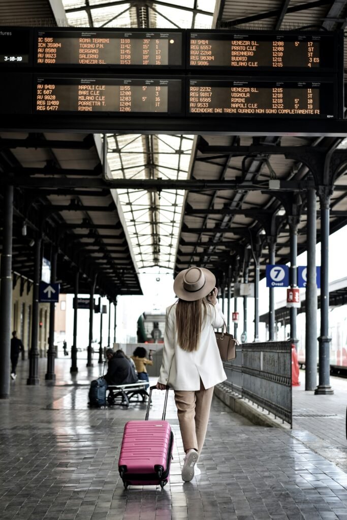 Mulher caminhando por um corredor de aeroporto, segurando uma mala de viagem cor de rosa, com luz natural entrando pelas janelas.