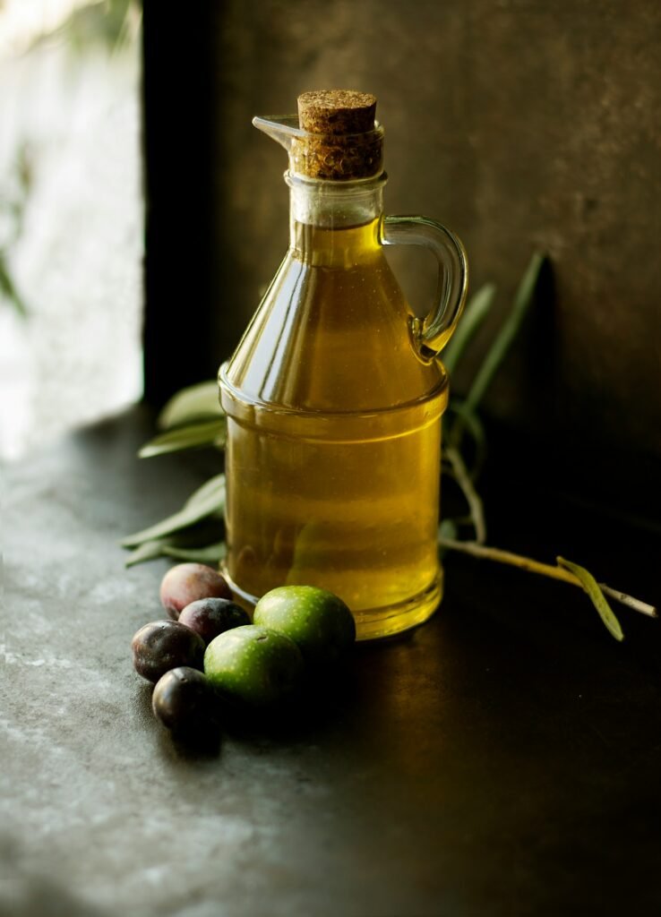 Garrafa de azeite de oliva exposta sobre uma bancada rústica, ao lado de azeitonas frescas e folhas de oliveira.