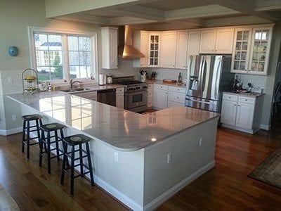 Cozinha em formato G com armários e bancadas brancas, banquetas pretas modernas e iluminação natural destacando o design clean.