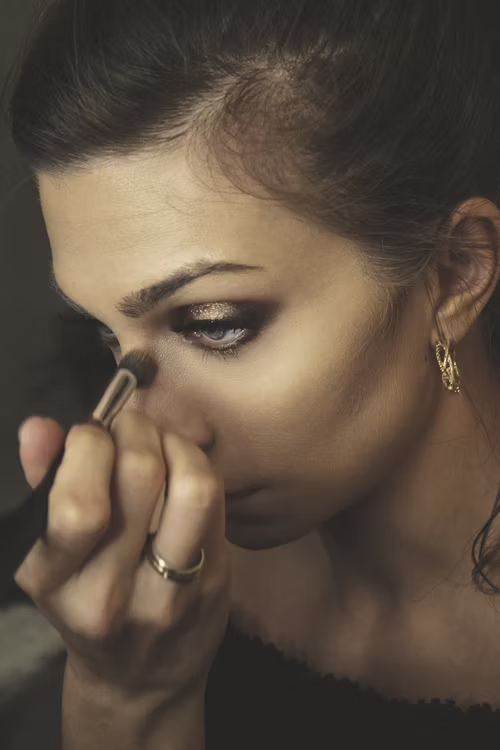 A imagem mostra uma mulher loira de olhos azuis vestindo uma blusa branca simples e elegante. Ela usa uma maquiagem neutra — com tons terrosos suaves, base leve, blush discreto e lábios em tom nude — que realça sua beleza natural sem exageros. A estética da imagem é leve, minimalista e transmite sofisticação, sendo ideal para representar autocuidado, moda básica ou beleza consciente. Imagem editada por She Lillas. Créditos: Unsplash, 2025.