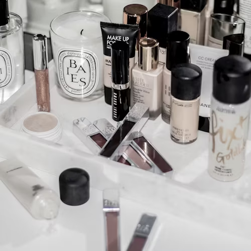 Bancada branca com diversos produtos de maquiagem organizados, incluindo pincéis, sombras, bases, batons e iluminadores.