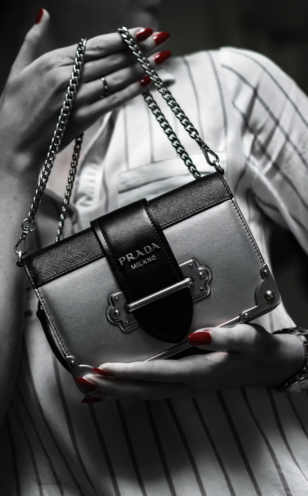 Mulher exibindo uma bolsa da Prada em uma imagem em preto e branco, com foco no acessório de luxo.
