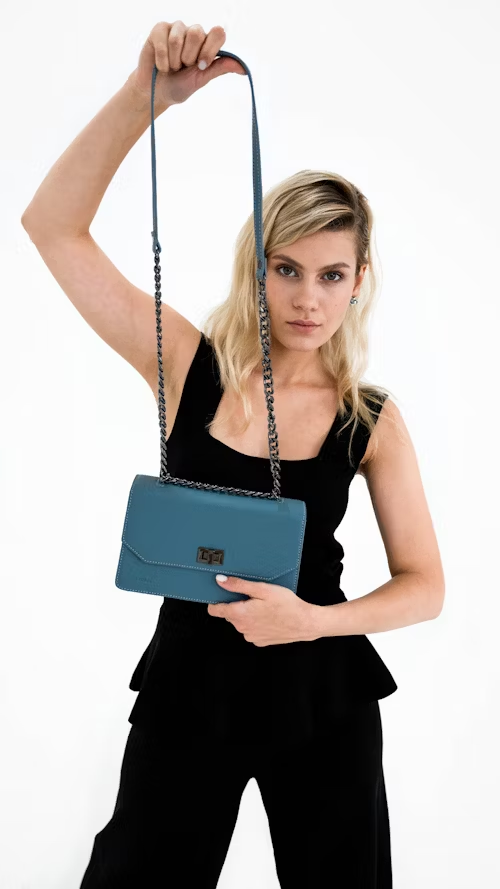 Mulher com roupa preta exibindo uma bolsa azul claro com alça de corrente prata.