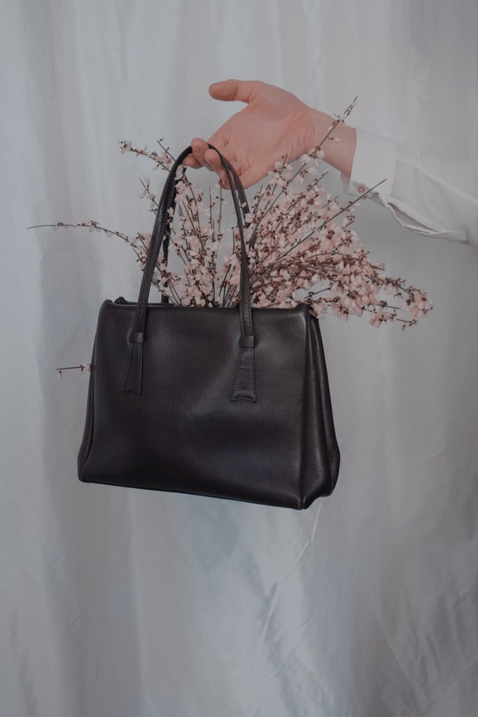 Bolsa preta com ramos de flores saindo de dentro, posicionada sobre fundo branco.