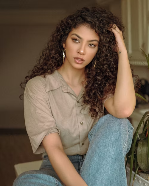 Mulher sentada posa para a foto com as mãos no cabelo, em atitude confiante.