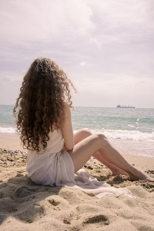 Mulher sentada na areia da praia observa o mar em um momento de contemplação.