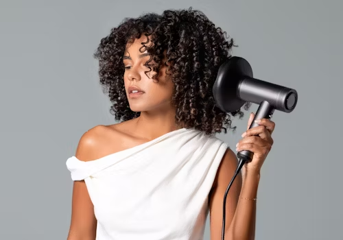 Mulher com blusa branca seca os cabelos com um difusor, modelando os cachos.