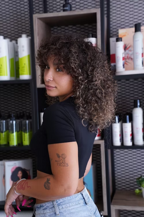 Mulher com cabelos crespos observa produtos em uma loja de cosméticos capilares.