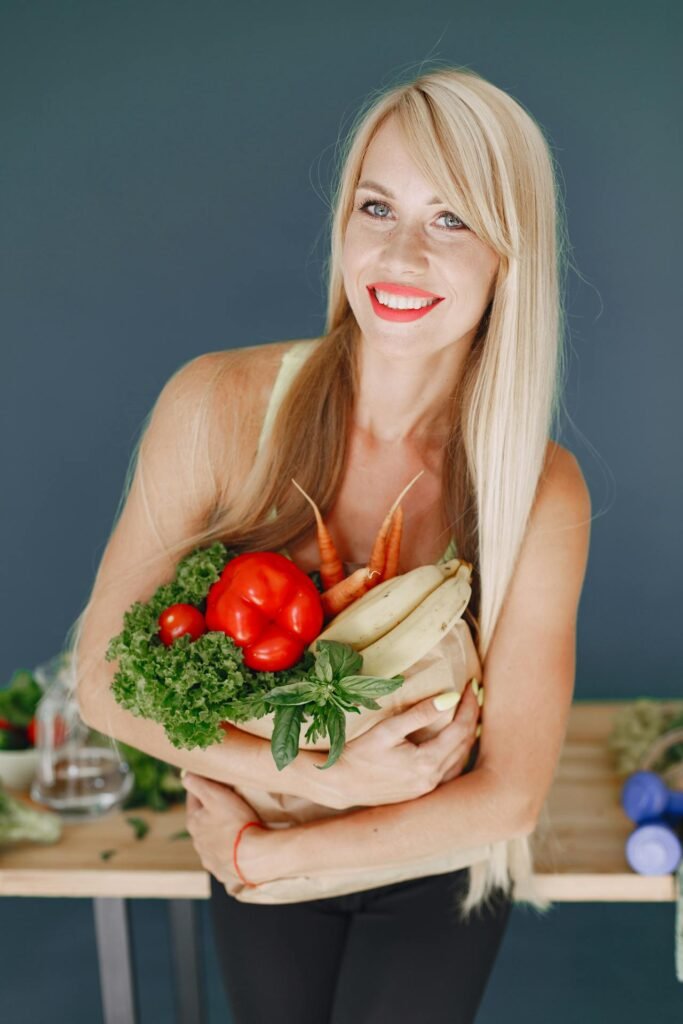 Mulher sorridente com cabelos brilhantes segurando um saco de papel cheio de alimentos saudáveis como vegetais, frutas e grãos.