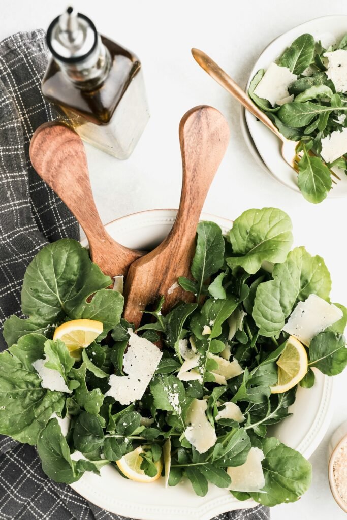 Prato de salada fresca com pegadores de madeira rústicos, ao lado de uma garrafa de azeites de Portugal sobre uma mesa natural.