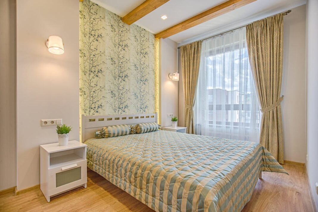Quarto decorado com papel de parede floral na cabeceira da cama, com roupas de cama claras e detalhes aconchegantes.