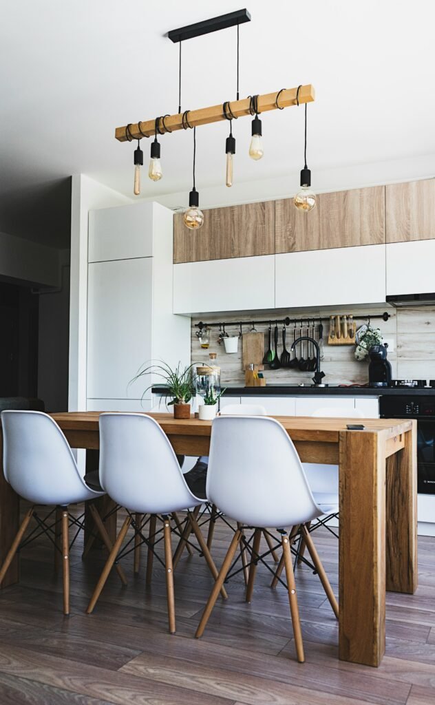 Cozinha com layout direto, mesa central com cadeiras e luminárias pendentes sobre a mesa.