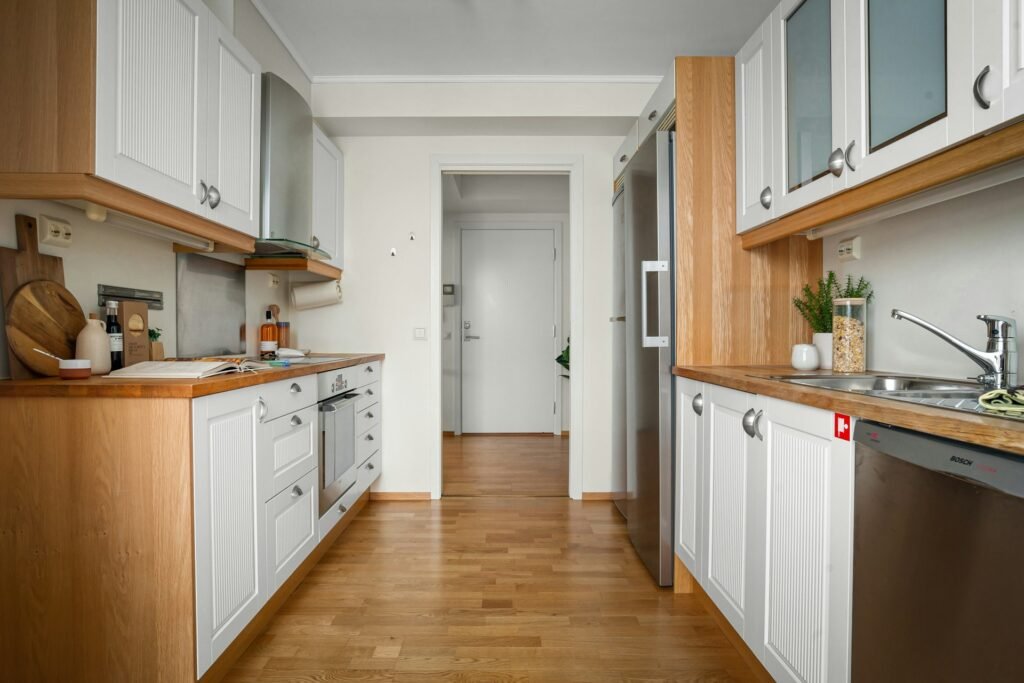 Cozinha de corredor com armários brancos, detalhes em madeira e utensílios modernos dispostos de forma organizada.